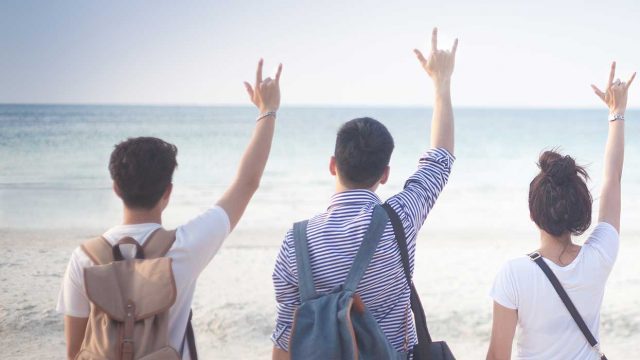 The backs of 2 males and 3 females looking out towards the beach holding up a hand sign, custom travel