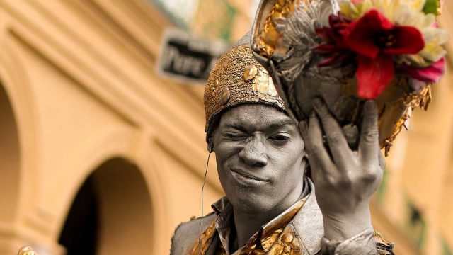 New Orleans street performer in gray body paint and gold costume holding flowers, new orleans performance tours