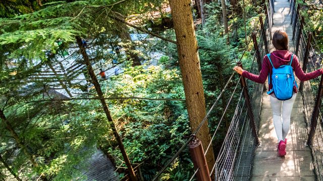 Girl dress in maroon jacket, white leggings, and pink shoes walking across a bridge on a hiking trail in the woods, vancouver victoria performance tours